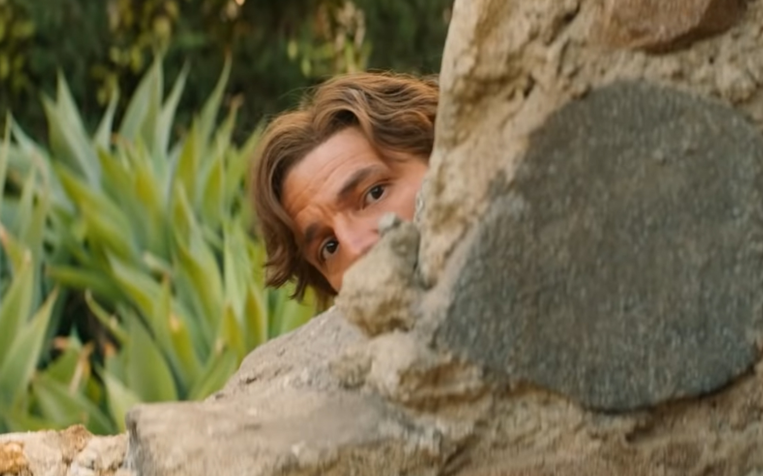 Pedro Pascal looks out from behind a stone wall