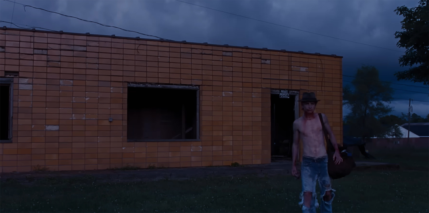 Timothée Chalamet walks away from a building with blood down his chest.