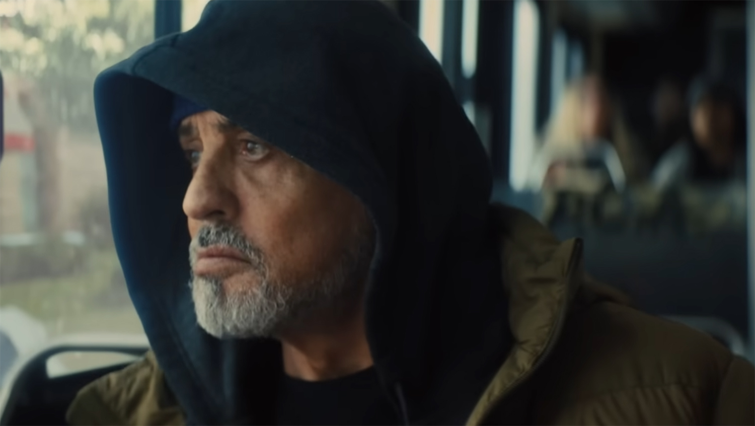 Stallone looks pensively out of a bus window.