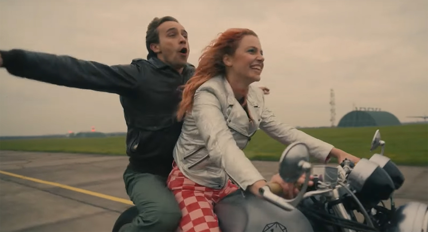 Niko and Marta ride on a motorbike down a runway.