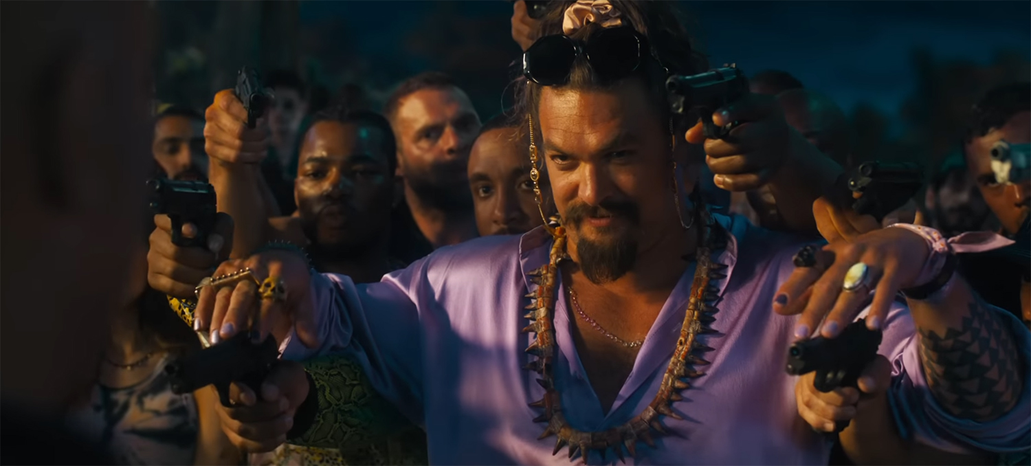 Jason Momoa postures with guns drawn.