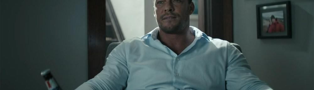 Alan Ritchson in a suit, drinking a bear.