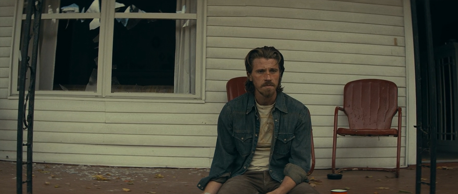 Russell sits with a ruined house behind them.