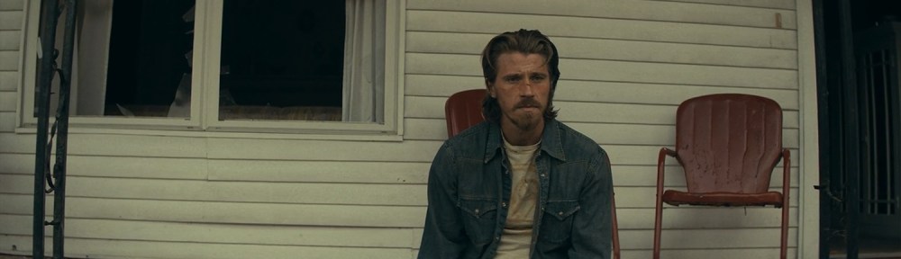 Russell sits with a ruined house behind them.