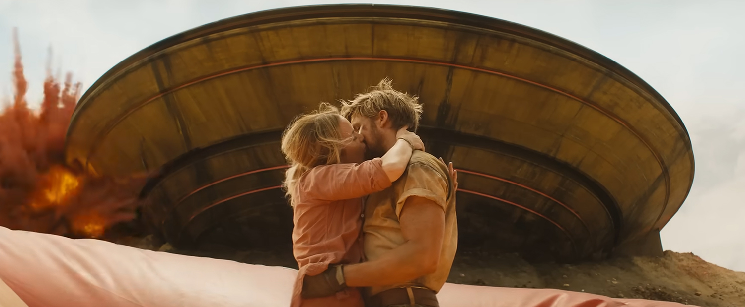 Ryan and Emily kiss as explosions in the background.