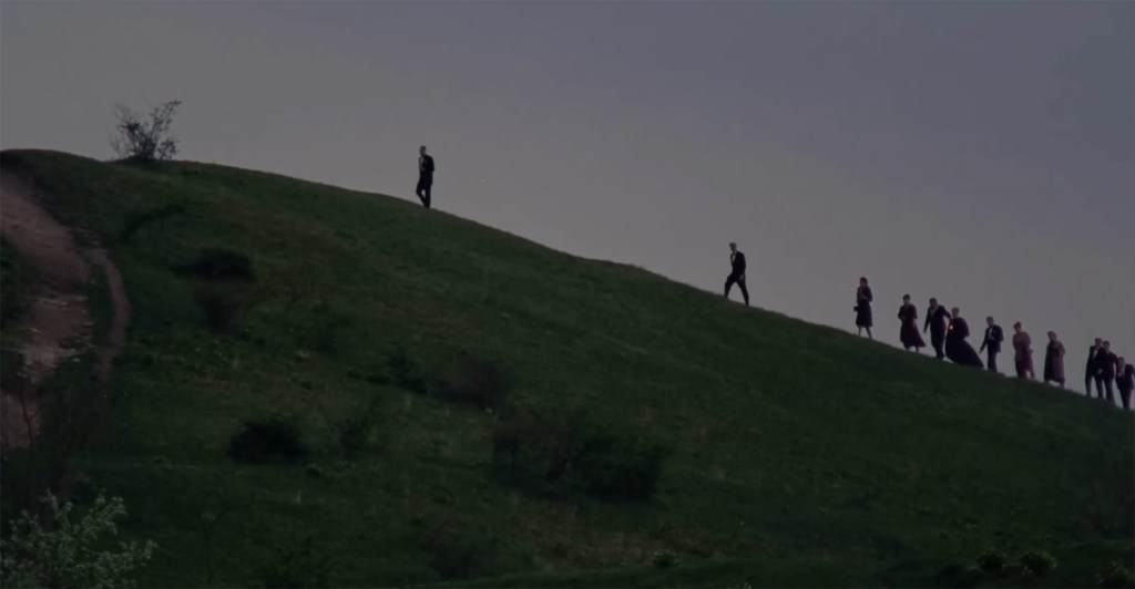 People walk up the side of a hill after the sun has set. 