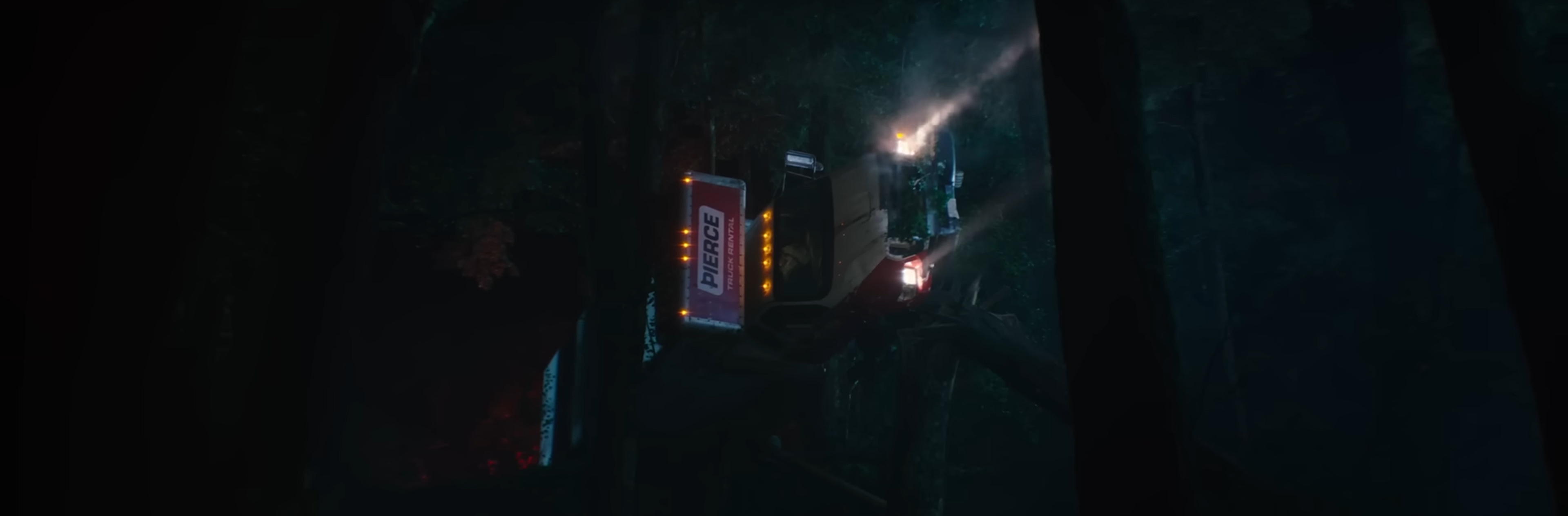 A truck hangs horizontally, held up by some trees.