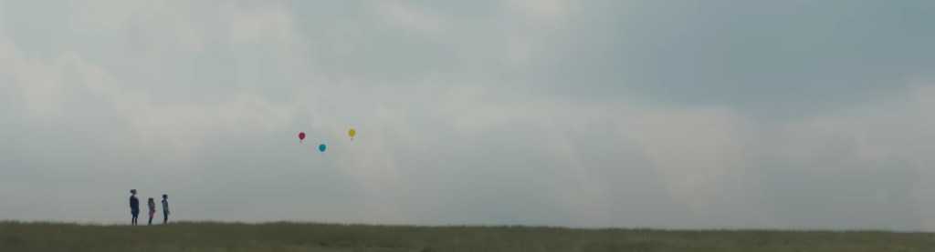Three figures release a single balloon into the air. 