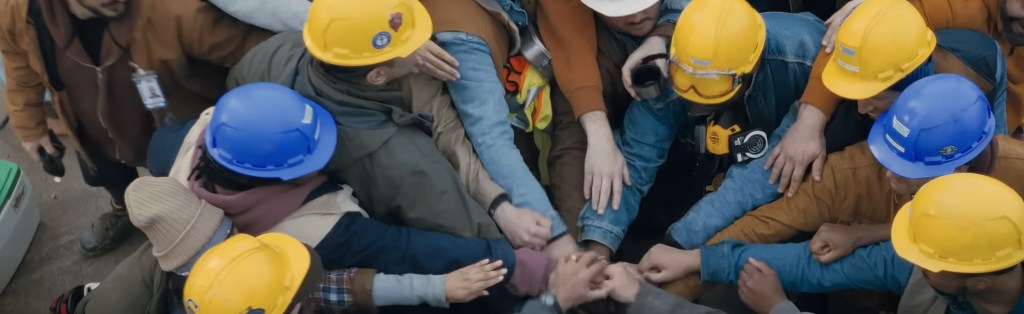 A bunch of men in hardhats but their hands in the middle. 