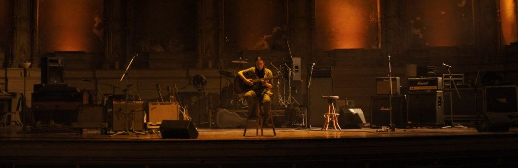 Ellie playing a guitar on the theatre stage.