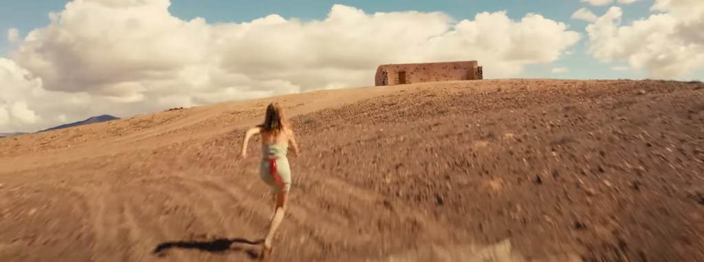 A woman running towards a cabin in the desert. 