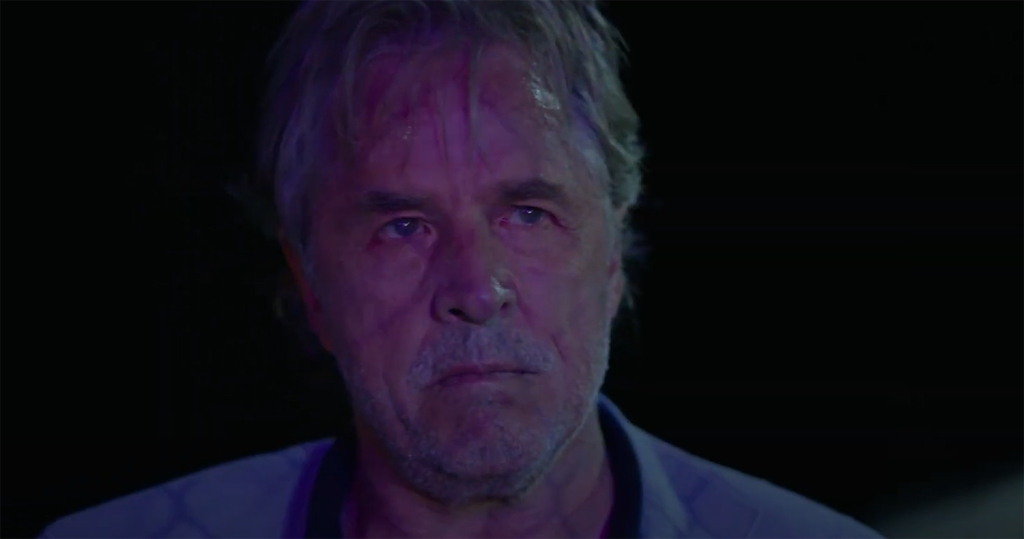 Don Johnson standing with a dour look on his illuminated face. 