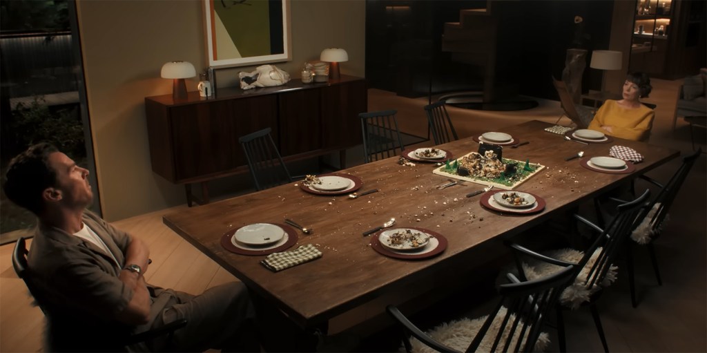 Benedict Cumberbatch and Olivia Colman looking across at each other across a ruined table. 