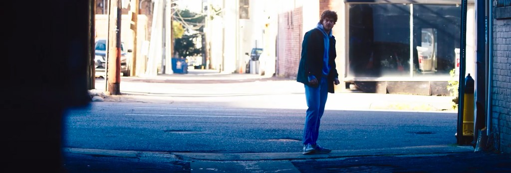 Jack Quaid standing in the middle of an alley. 