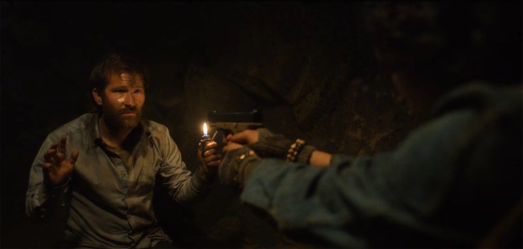 A woman holds a man up with a gun. 