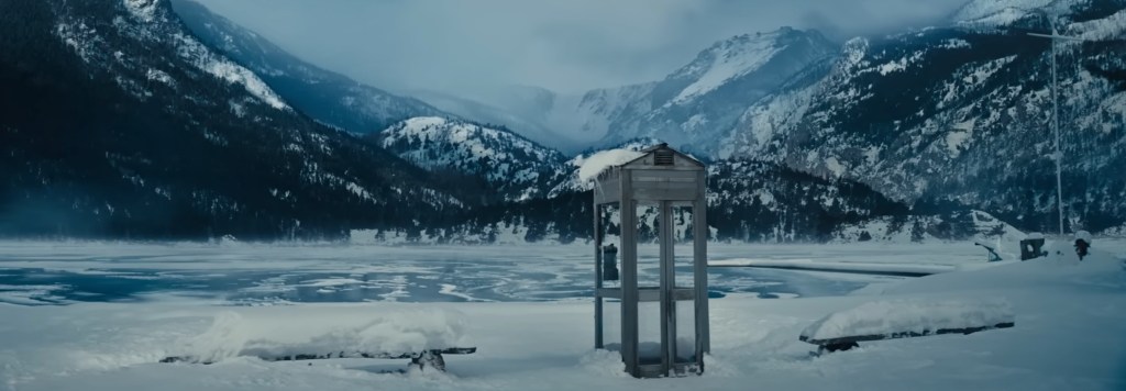 A pay phone sitting by a lake covered in snow. 