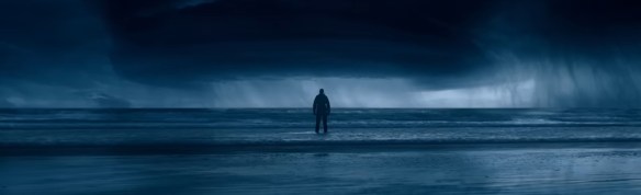 A man looking out to a storm coming in over the ocean.