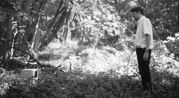 A man looks at a computer in the woods (it is not meant to be there).