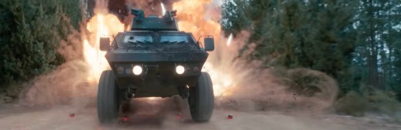 A military car driving with explosions behind it. 