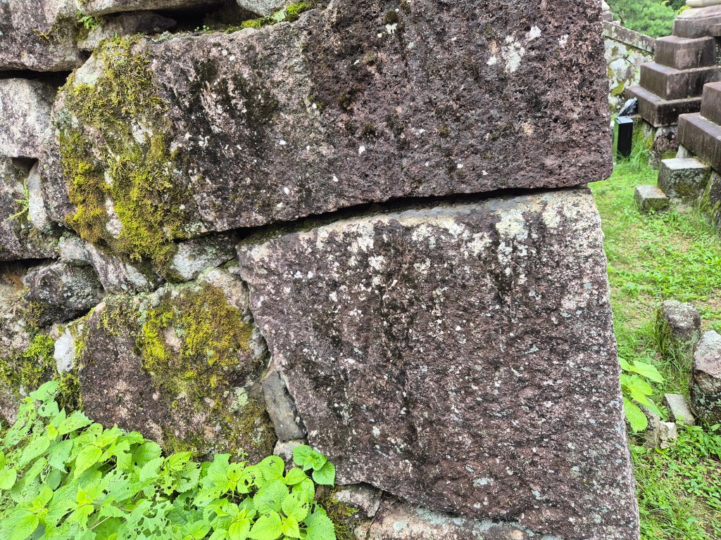 Close-up of an ancient stone wall showing weathered, moss-covered blocks and greenery at the base.