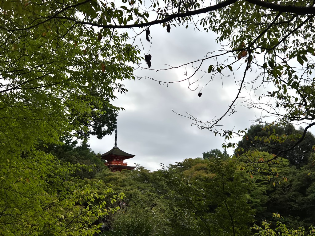 A traditional Japanese pagoda partially obscured by lush green trees under a cloudy sky.