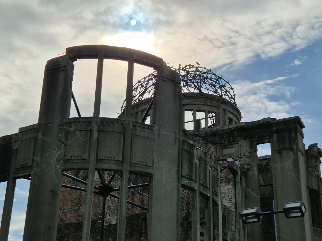 Ruins of a historic building under a cloudy sky, with the sun partially visible above.