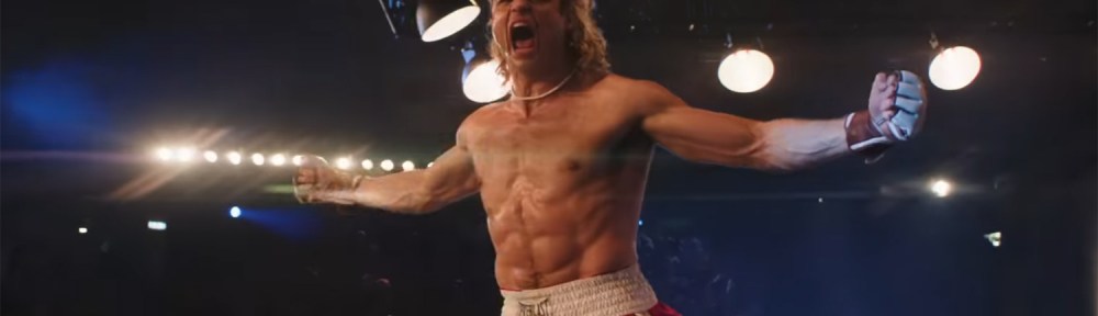 Noah Centineo yelling arms outstretched on the edge of a fighting ring.