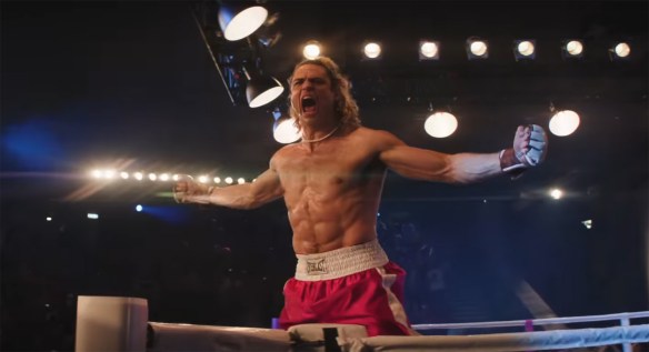 Noah Centineo yelling arms outstretched on the edge of a fighting ring.